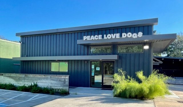 Exterior view of Peace Love Dogs modern pet training facility with large signage in Houston, Texas, under clear blue sky.